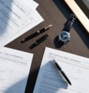 Flat lay of luxury estate planning documents on a dark wooden desk with a fountain pen and wristwatch, symbolising structured financial preparation