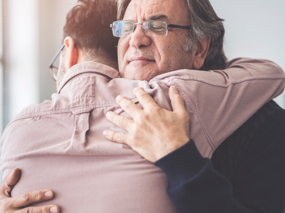 Older man hugging son in a moment of gifting a living inheritance.