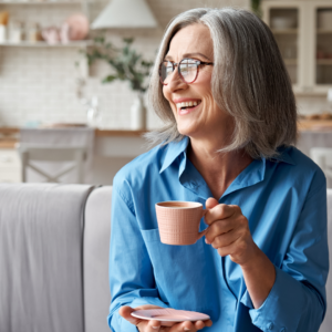 over 55-year-old woman sitting on the sofa, holding a coffee and smiling