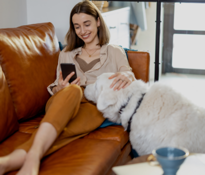Woman smiling on the sofa, looking at her phone while stroking her dog