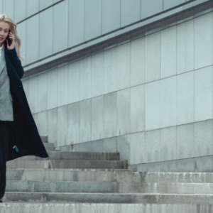 A professional woman walks down a set of modern city steps while speaking on her mobile phone. Dressed in a navy coat and tailored attire, she appears focused and composed, representing the pace and demands of a legal career.