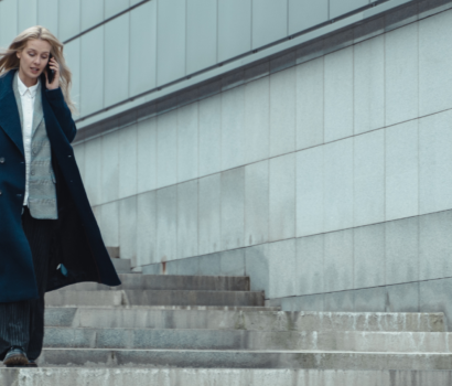 A professional woman walks down a set of modern city steps while speaking on her mobile phone. Dressed in a navy coat and tailored attire, she appears focused and composed, representing the pace and demands of a legal career.