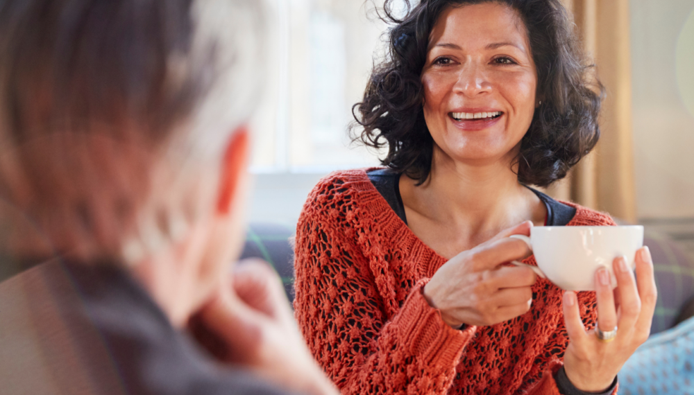 Smiling woman holding a cup of tea during a relaxed later life lending conversation at home.