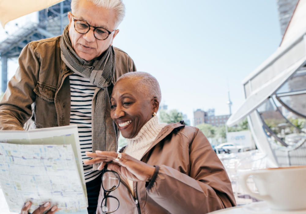 Smiling retired couple reviewing a map at a café during a city break, enjoying later life freedom