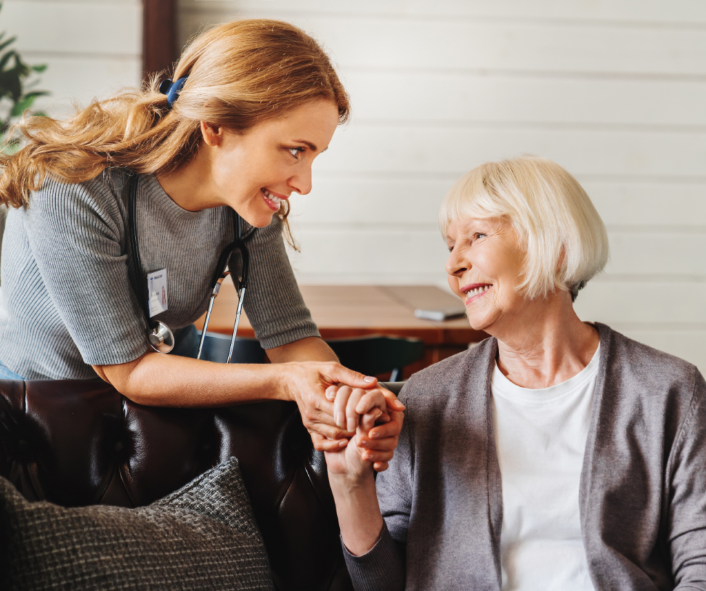 A smiling healthcare professional holding hands with an elderly woman at home, symbolising trust, personalised care, and long-term health support in later life.